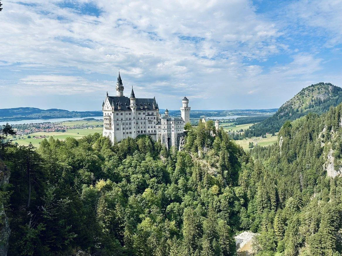 Neuschwanstein Castle rising above forest with the Bavarian Alps behind it