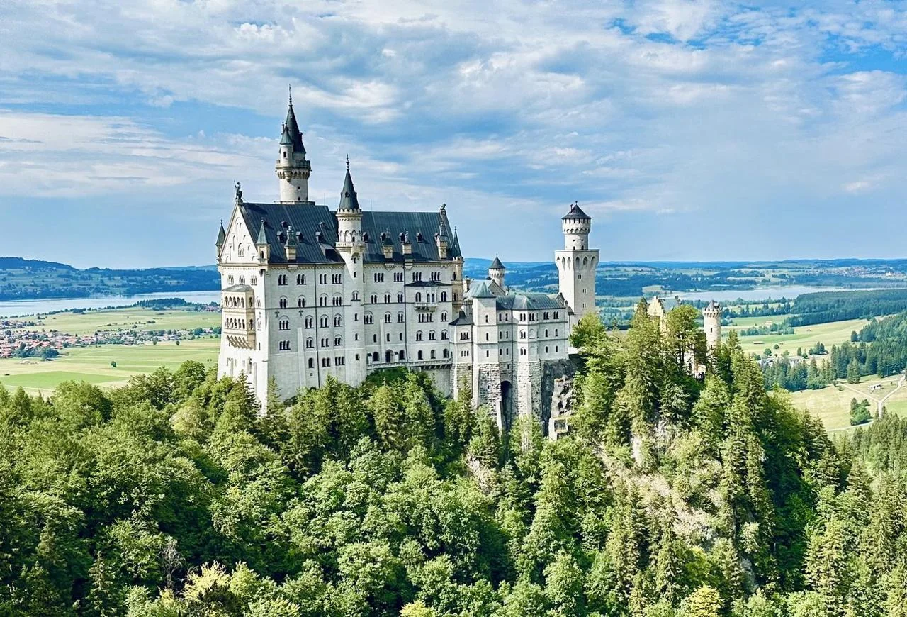 Neuschwanstein Castle surrounded by green hills and distant Alps